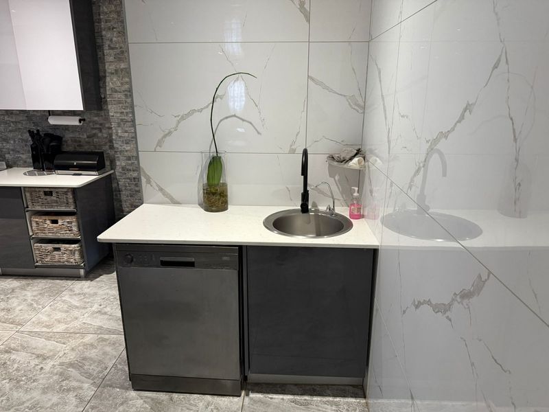 Modern scullery area featuring sleek dark cabinetry, stone countertops, a stainless steel sink with a black mixer tap, and elegant marble-look wall tiling.