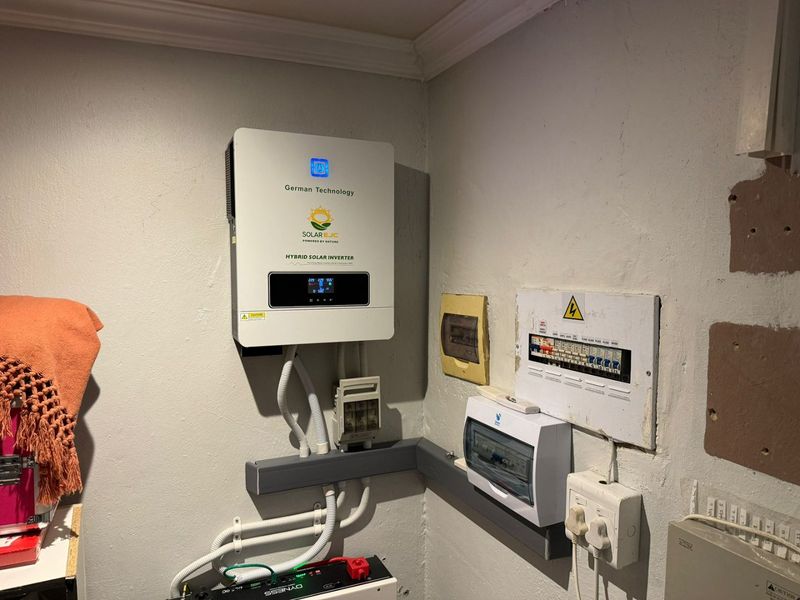Utility area featuring a wall-mounted hybrid solar inverter and electrical distribution board setup with visible conduit and power infrastructure.