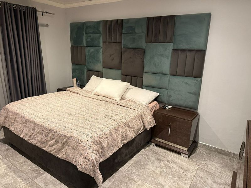 A well-maintained bedroom featuring large-format tiled flooring and a prominent, custom-upholstered wall-mounted headboard.