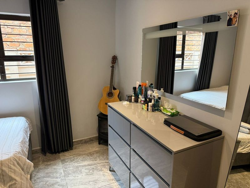 A well-maintained bedroom featuring modern tiled flooring, a large wall-mounted mirror, and secure window treatments.