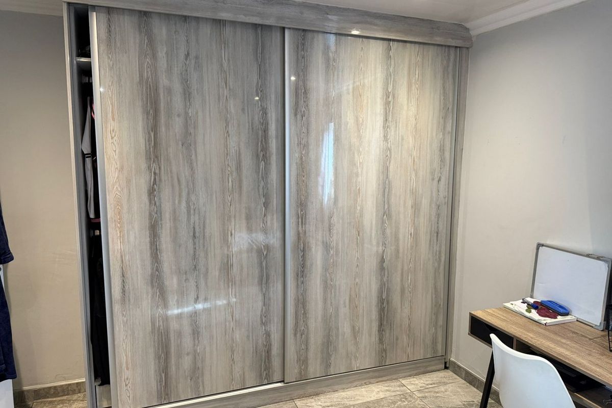 A bedroom featuring a modern wood-grain finish built-in sliding door wardrobe, recessed ceiling lighting, and neutral tiled flooring.