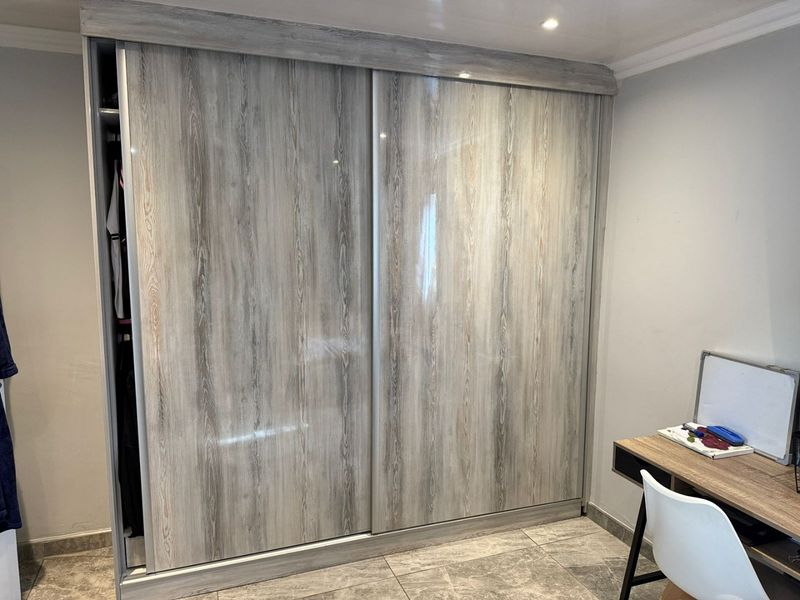 A bedroom featuring a modern wood-grain finish built-in sliding door wardrobe, recessed ceiling lighting, and neutral tiled flooring.