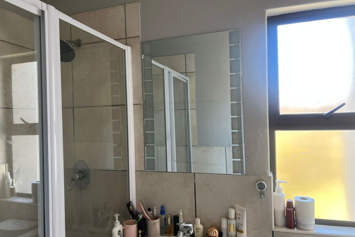 A functional bathroom featuring a shower enclosure, wall-mounted mirror, and tiled splashback, providing essential amenities in a compact layout.