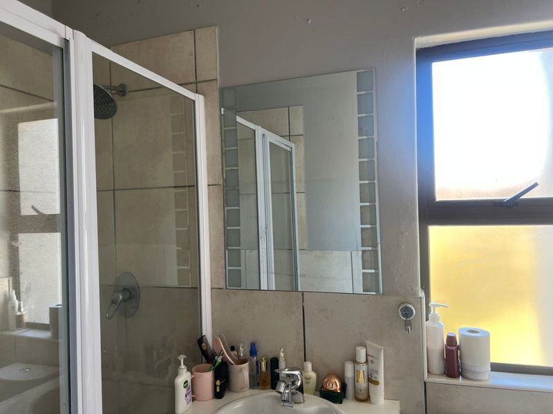 A functional bathroom featuring a shower enclosure, wall-mounted mirror, and tiled splashback, providing essential amenities in a compact layout.