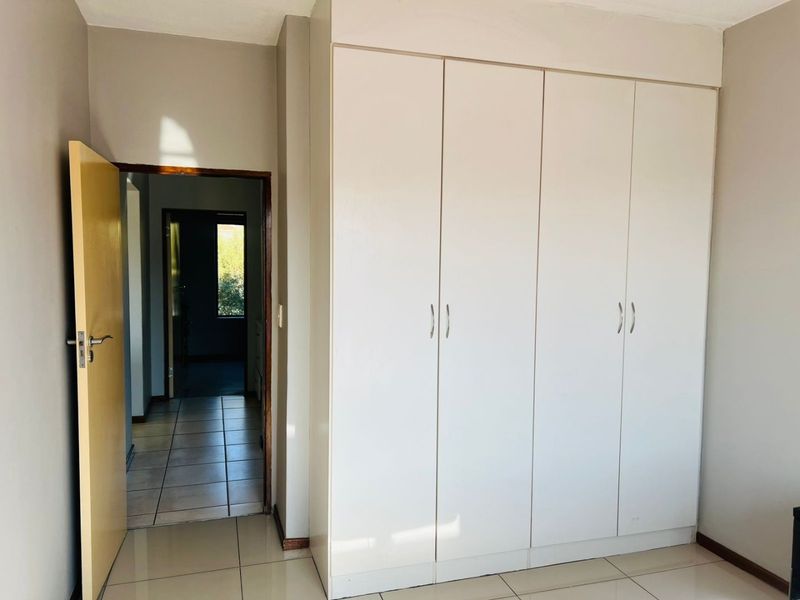 A clean, empty bedroom featuring neutral tiled flooring and a large, white built-in wardrobe with ample storage space.