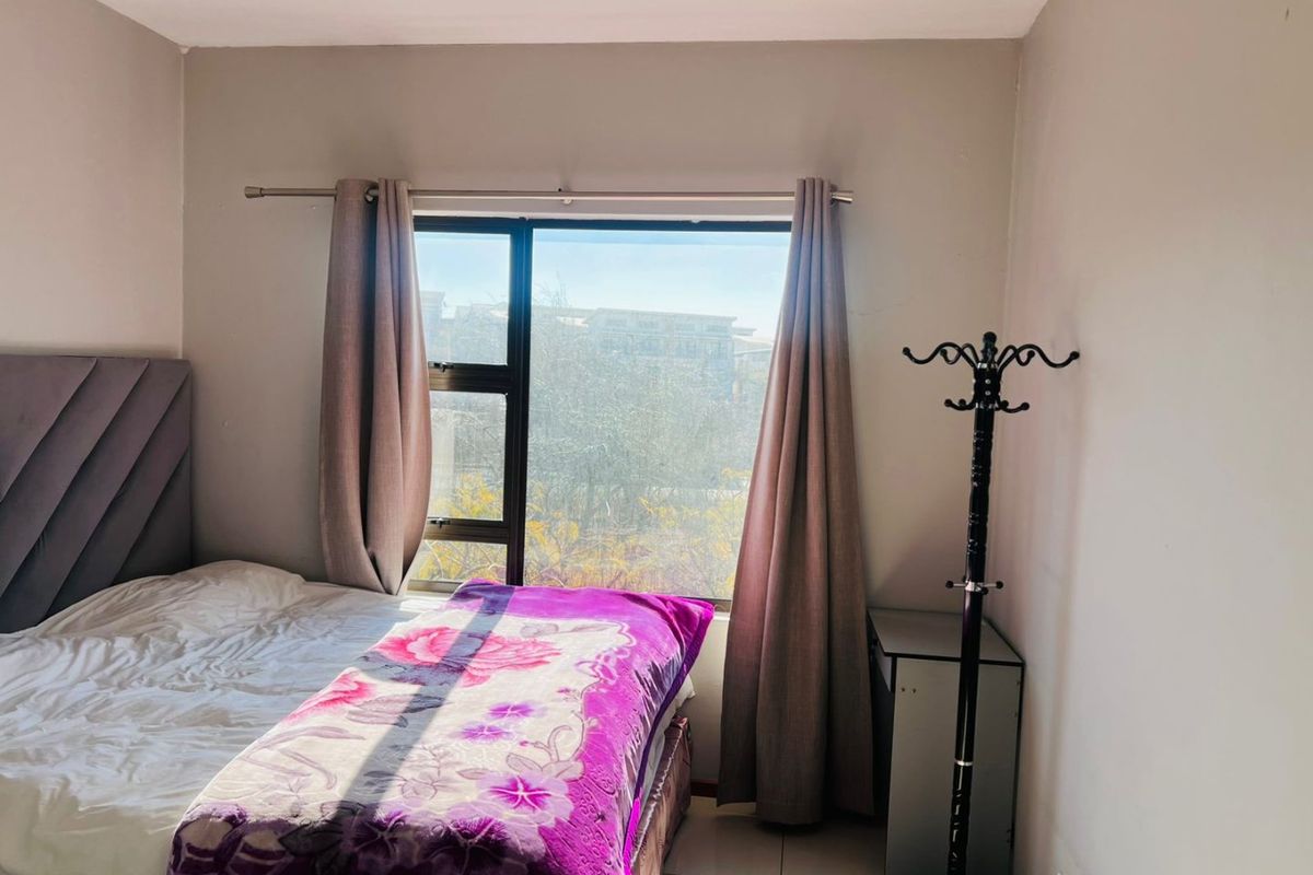 A bedroom featuring tiled flooring and a large aluminium-framed window providing natural light.