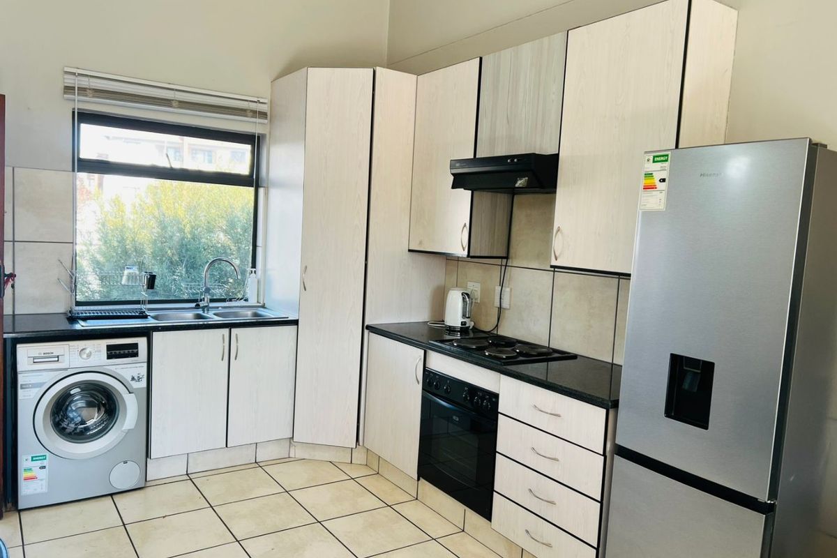 Functional kitchen featuring light-toned cabinetry, dark laminate countertops, built-in oven with hob, extractor fan, and integrated space for a washing machine.