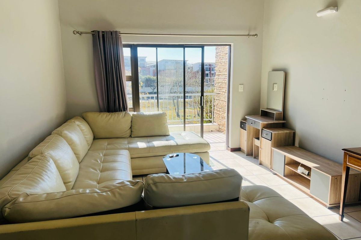 A bright living room featuring tiled flooring and a large sliding glass door that provides access to an outdoor balcony area.