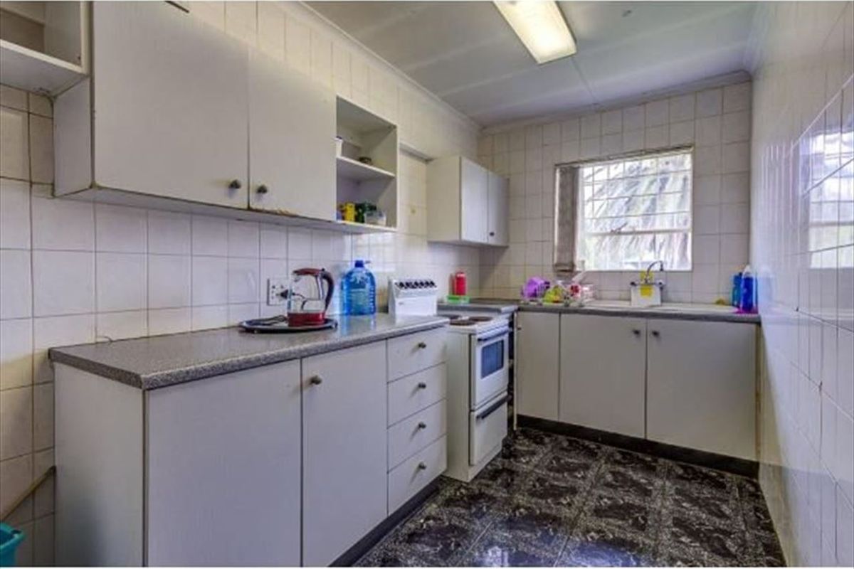 A functional kitchen featuring built-in cabinetry, laminate countertops, a freestanding stove, and tiled finishes throughout, offering potential for modernization.