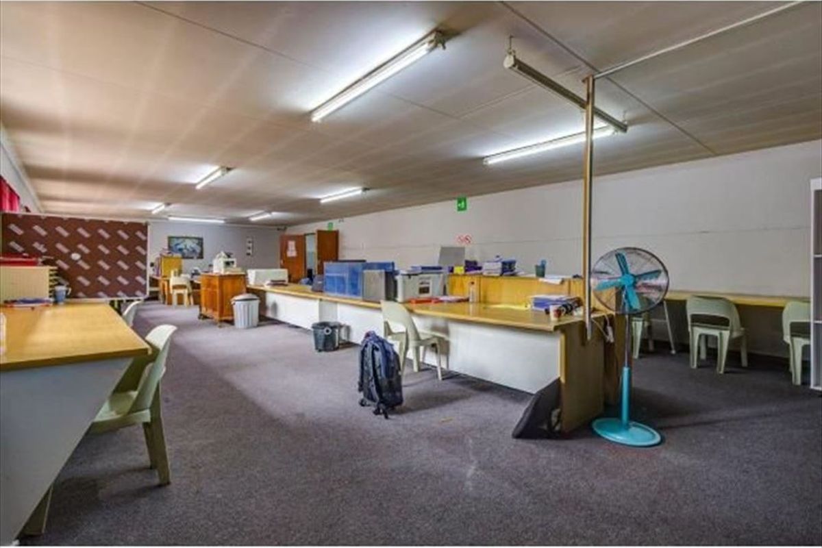 A spacious commercial office area featuring built-in desk workstations, fluorescent lighting, and carpeted flooring, suitable for a collaborative work environment.