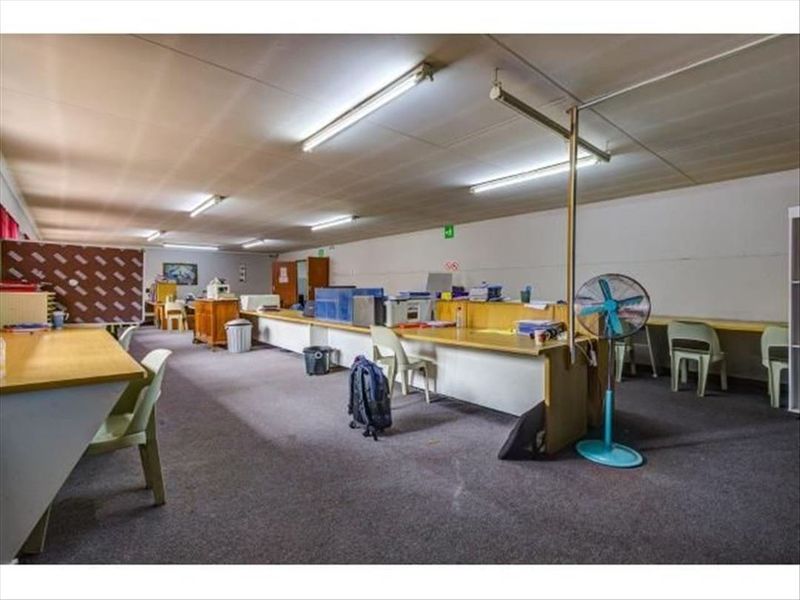 A spacious commercial office area featuring built-in desk workstations, fluorescent lighting, and carpeted flooring, suitable for a collaborative work environment.