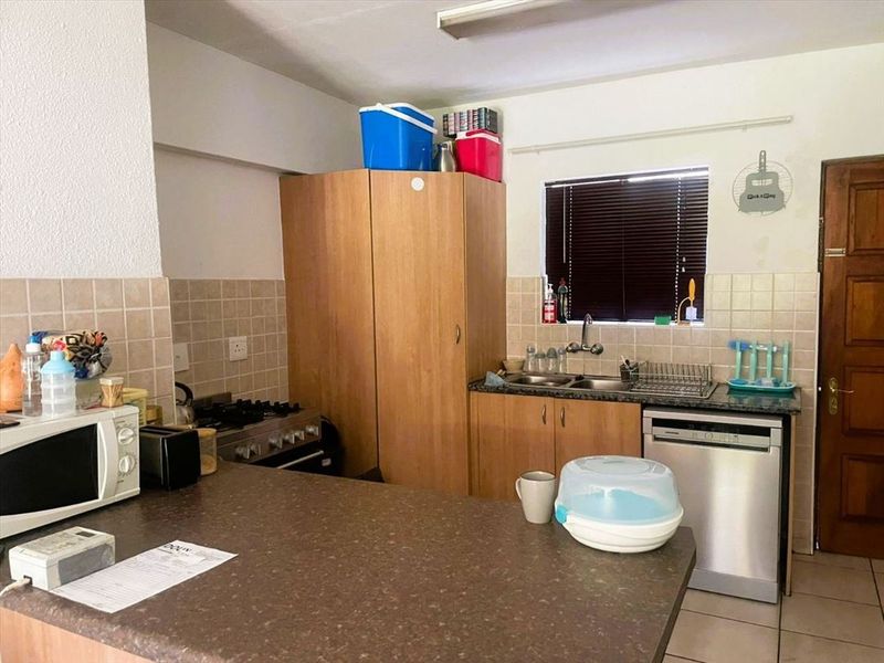 A functional kitchen featuring built-in wooden cabinetry, a gas hob, tiled backsplash, and a double sink with a window view.