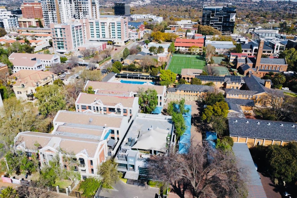 Aerial view of a commercial property complex featuring multiple buildings, swimming pool, tennis courts, and landscaped grounds in an urban setting.