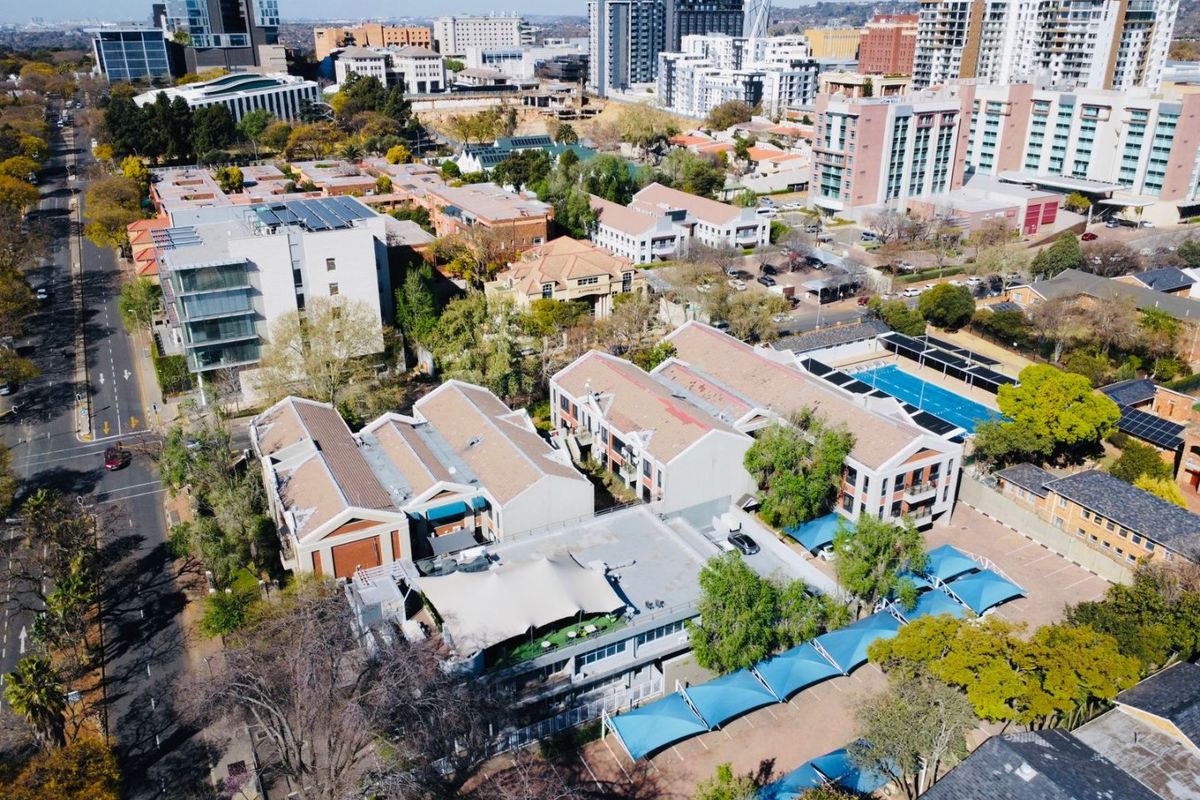 Aerial view of a commercial property complex featuring multiple buildings, a swimming pool, and covered parking areas within an urban setting.