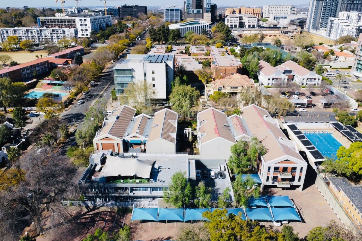Aerial view of a commercial property complex featuring multiple buildings, paved parking areas with shade sails, and an outdoor swimming pool.