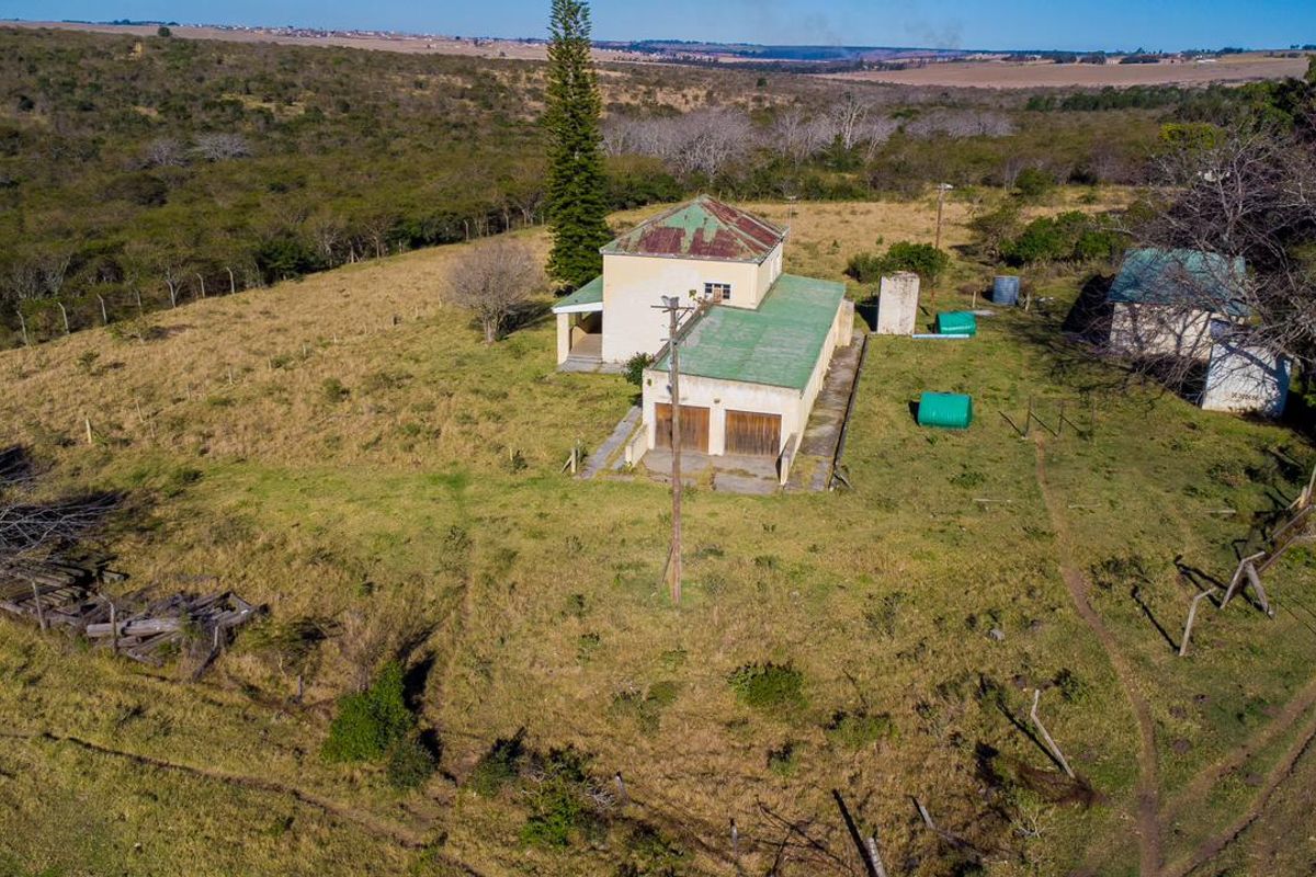 Aerial view of a rural farm property featuring a main dwelling with metal roofing, outbuildings, and expansive surrounding land.