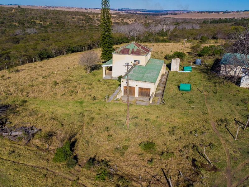 Aerial view of a rural farm property featuring a main dwelling with metal roofing, outbuildings, and expansive surrounding land.