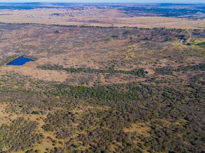 An expansive aerial view of the farm property, showcasing the vast natural landscape, open veld, and a small dam.