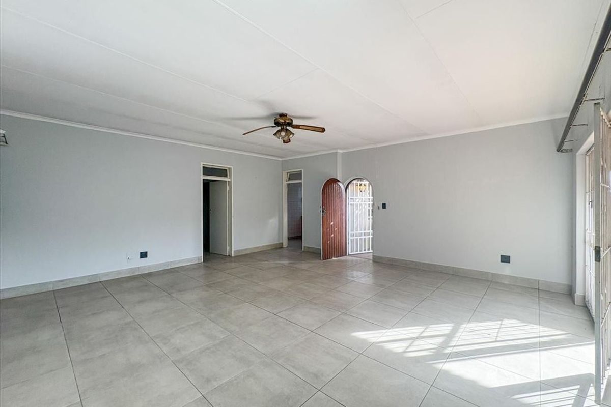 A spacious, empty living area featuring neutral tiled flooring, a ceiling fan, and an arched entrance with a security gate.