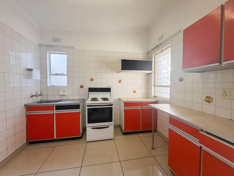A functional kitchen featuring original cabinetry, a freestanding stove, tiled splashbacks, and tiled flooring, offering a blank canvas for modern renovation.