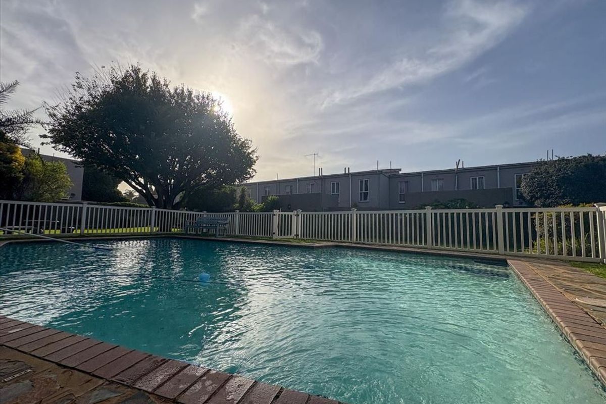 A well-maintained swimming pool area featuring brick coping and a white picket fence, set within a communal townhouse complex garden.