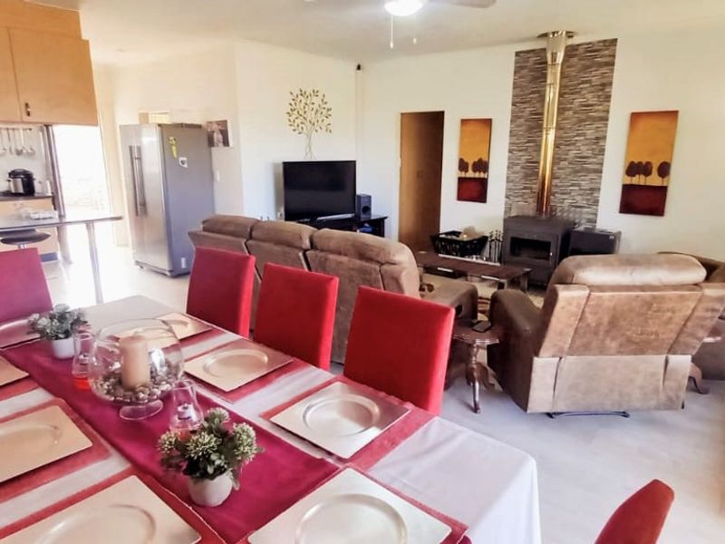 Open-plan living and dining area featuring a wood-burning fireplace with stone cladding, adjacent to a functional kitchen with built-in cabinetry.