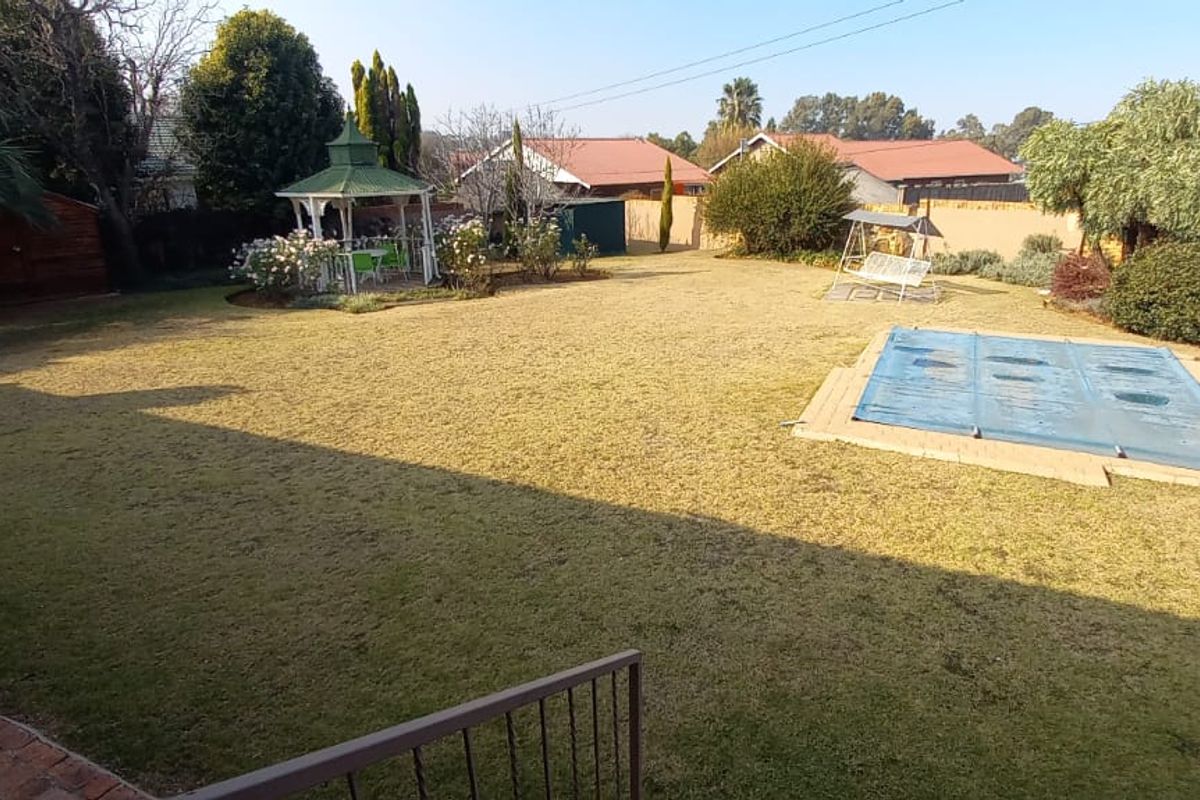 Spacious rear garden featuring a well-maintained lawn, a swimming pool with a cover, and a decorative gazebo in a quiet residential setting.