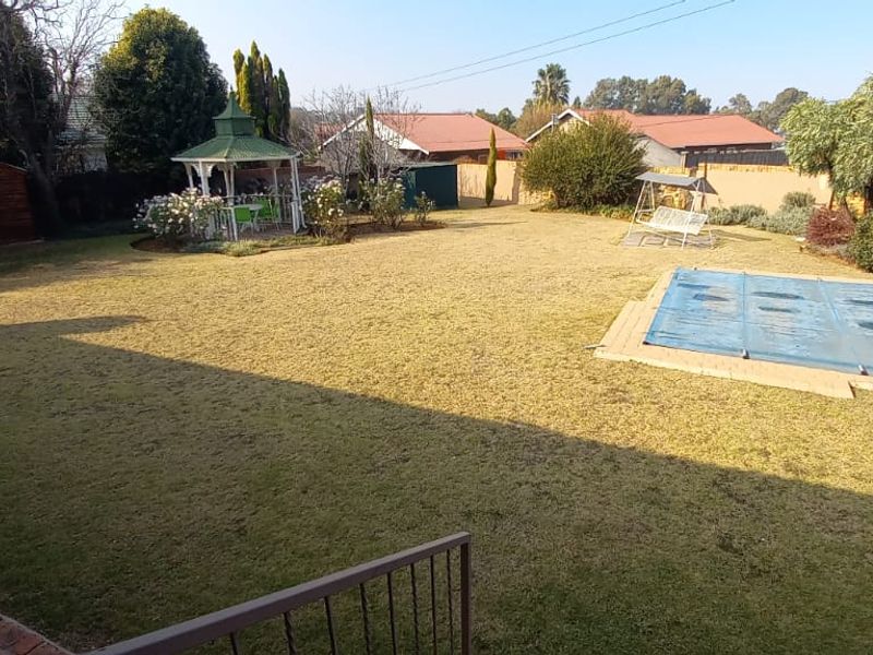 Spacious rear garden featuring a well-maintained lawn, a swimming pool with a cover, and a decorative gazebo in a quiet residential setting.