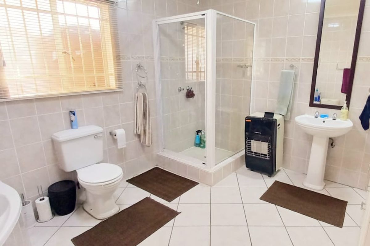 A functional bathroom featuring a pedestal washbasin, a separate shower enclosure, and a toilet, finished with neutral wall and floor tiling.