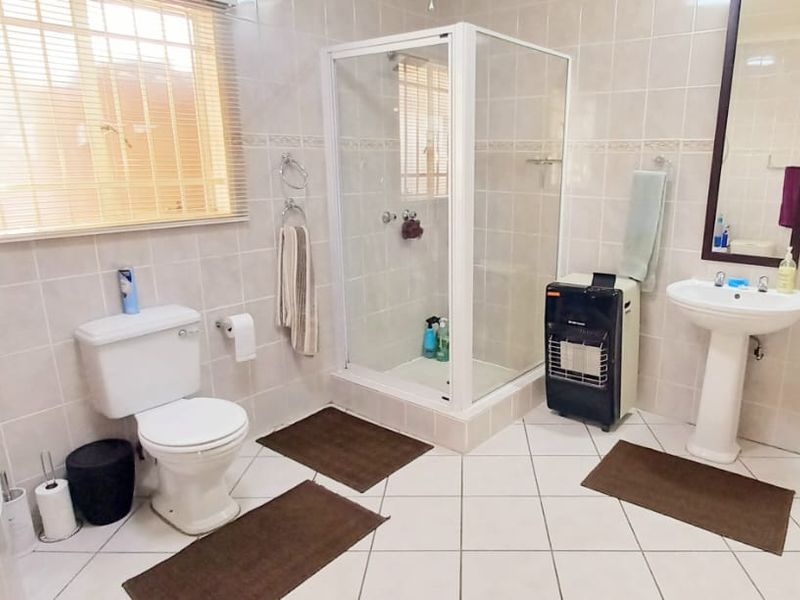 A functional bathroom featuring a pedestal washbasin, a separate shower enclosure, and a toilet, finished with neutral wall and floor tiling.
