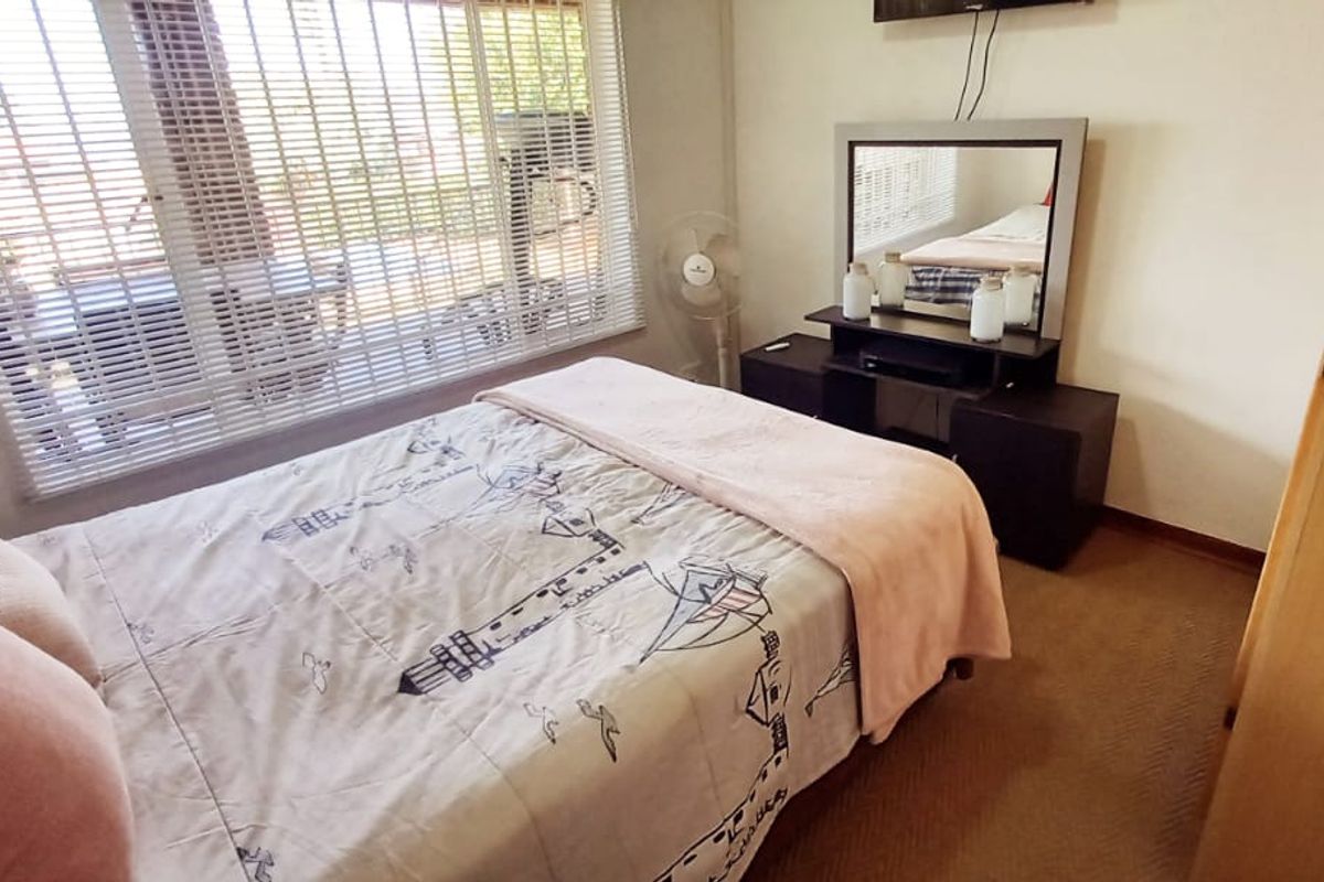 A functional bedroom featuring carpeted flooring, a built-in wardrobe, and large windows fitted with venetian blinds.