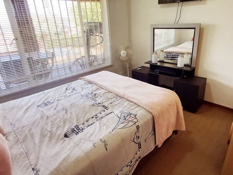 A functional bedroom featuring carpeted flooring, a built-in wardrobe, and large windows fitted with venetian blinds.