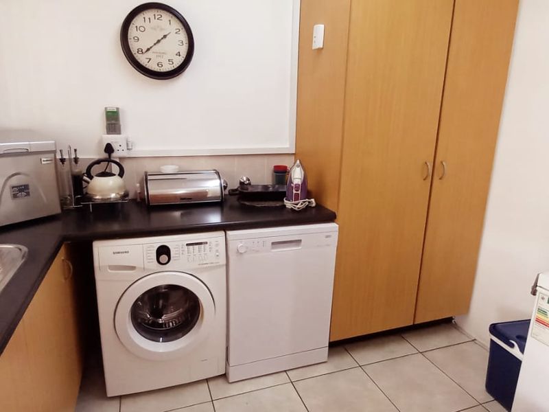 Functional laundry room featuring built-in cabinetry, laminate countertops, a stainless steel sink, and tiled flooring.