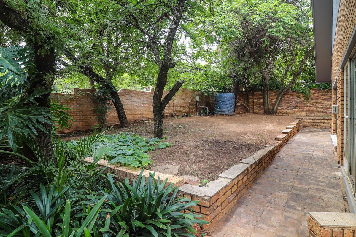 A private rear garden featuring a paved patio area, brick retaining walls, mature trees, and a perimeter brick boundary wall.