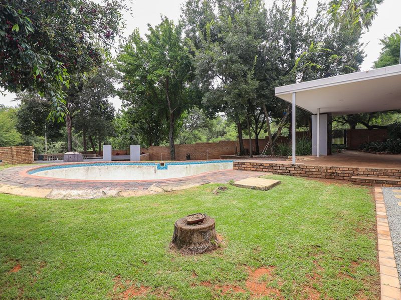Rear garden featuring a swimming pool with brick surround, a covered patio area, and established trees, requiring maintenance to the pool structure.
