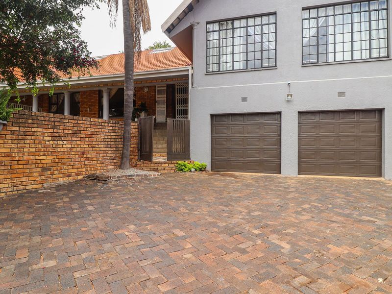 Front exterior view featuring a double garage, paved driveway, and brick boundary wall with a tiled roof structure.