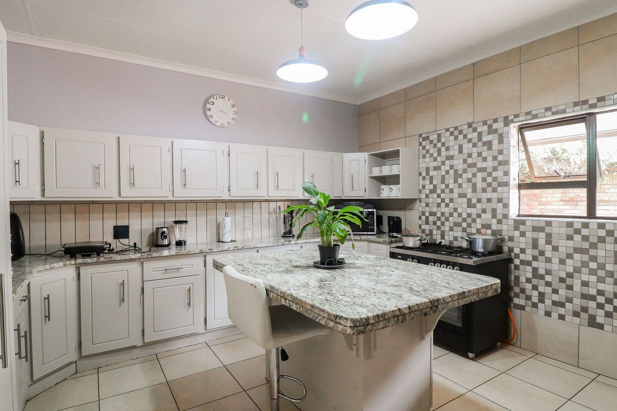 A well-maintained kitchen featuring granite countertops, a central island, gas stove, and ample built-in cabinetry with a decorative tiled backsplash.