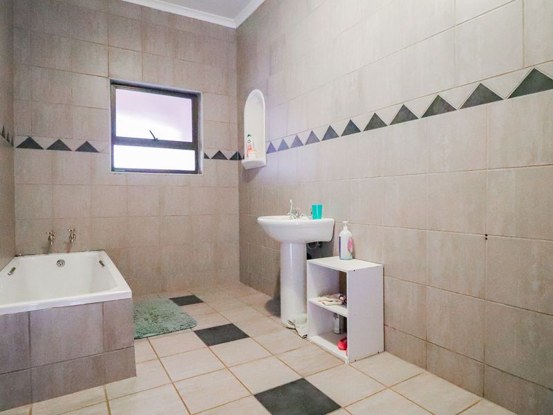 A functional bathroom featuring a built-in bathtub, pedestal basin, and neutral wall tiling with a decorative border.