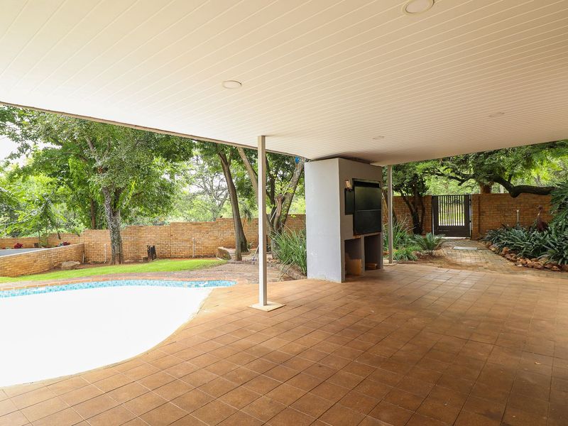 Covered outdoor patio area featuring a built-in braai, tiled flooring, and direct access to the swimming pool and garden.
