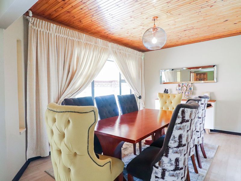 A dining room featuring a warm timber tongue and groove ceiling, laminate flooring, and a central pendant light fixture.