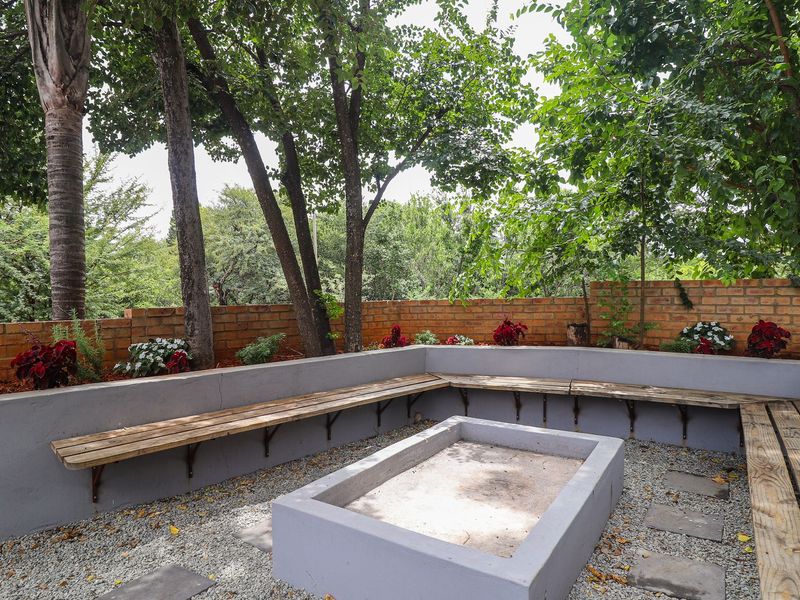 Outdoor entertainment area featuring a built-in fire pit and integrated bench seating, enclosed by a brick boundary wall in a landscaped garden setting.