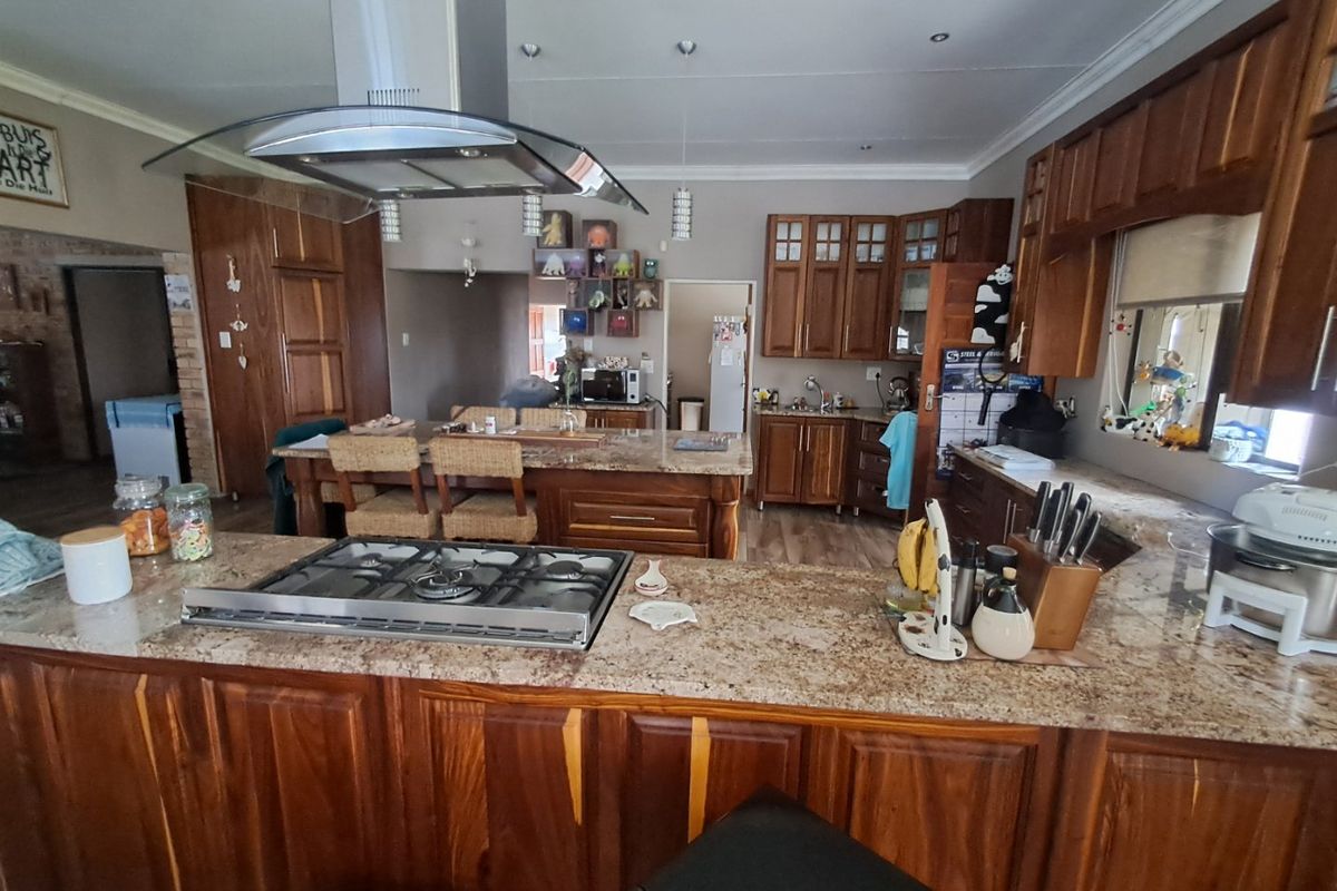 Spacious kitchen featuring extensive wooden cabinetry, granite countertops, a central island with a gas hob, and a stainless steel extractor fan.