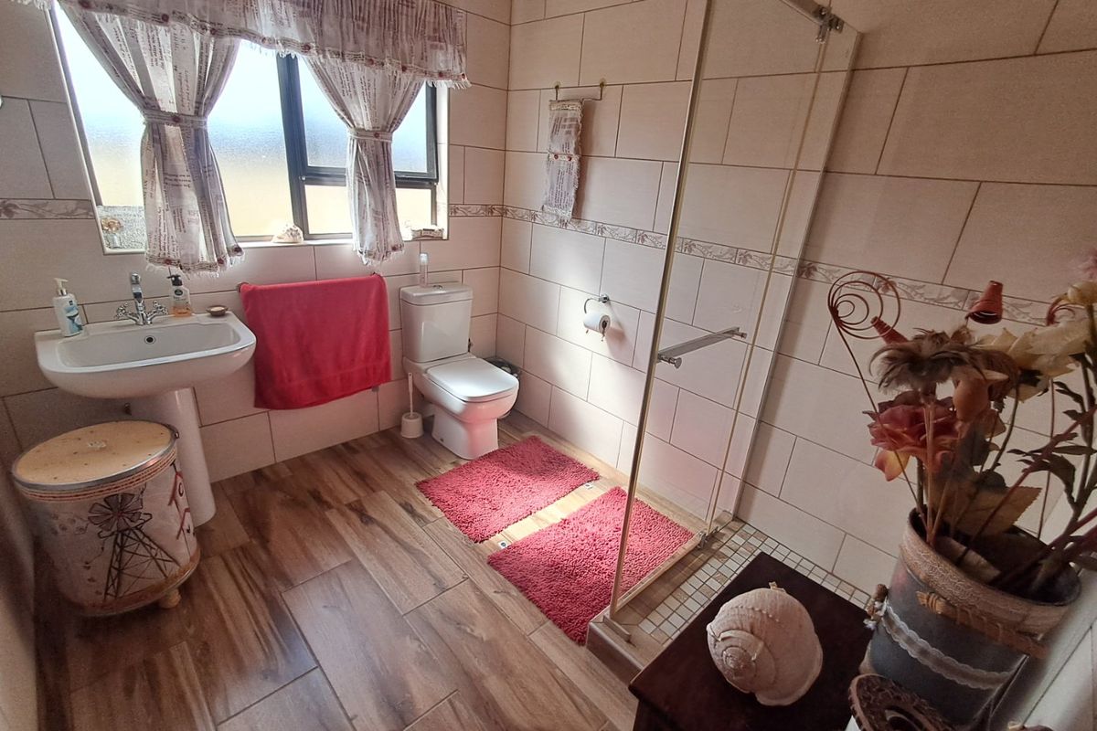 A functional bathroom featuring a pedestal washbasin, toilet, and a walk-in shower with a glass screen, finished with tiled walls and wood-look flooring.
