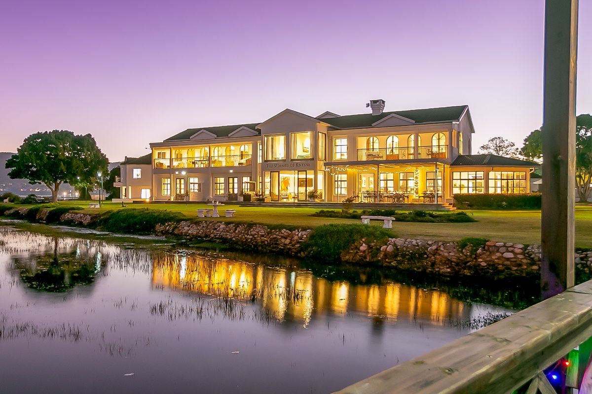 A stunning twilight view of a large commercial property featuring a stone retaining wall, expansive lawn, and illuminated multi-level facade with balconies.