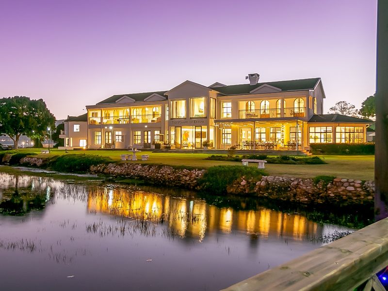 A stunning twilight view of a large commercial property featuring a stone retaining wall, expansive lawn, and illuminated multi-level facade with balconies.