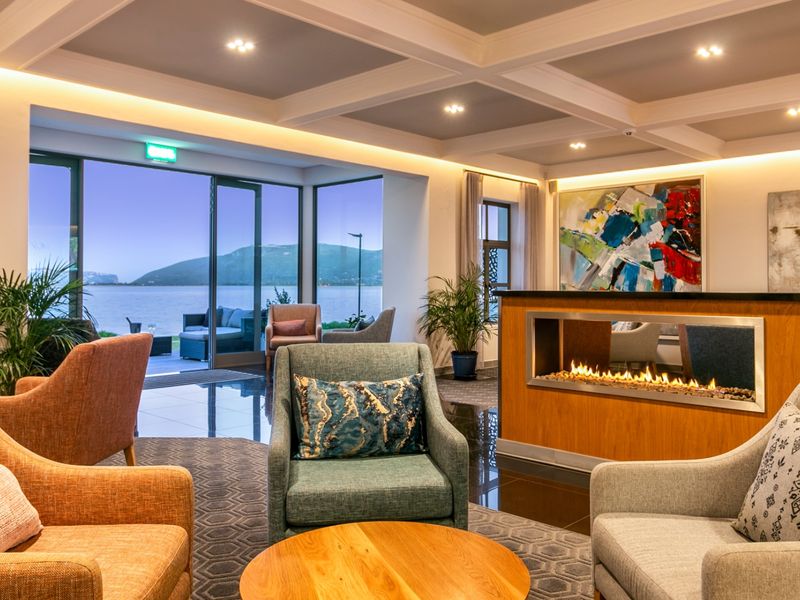 Elegant commercial lounge area featuring a modern built-in fireplace, coffered ceilings with recessed lighting, and expansive sliding glass doors offering scenic waterfront views.