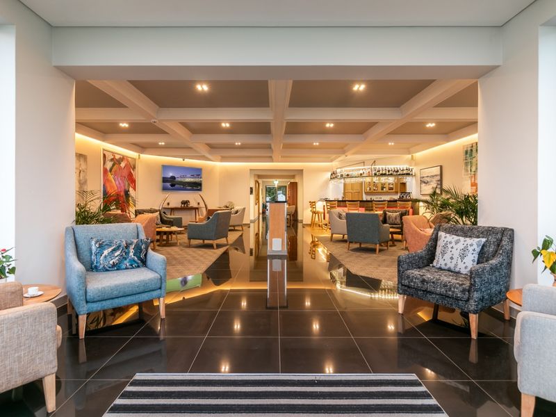 Spacious open-plan commercial lounge area featuring a coffered ceiling, recessed lighting, polished floor tiles, and a built-in bar counter.