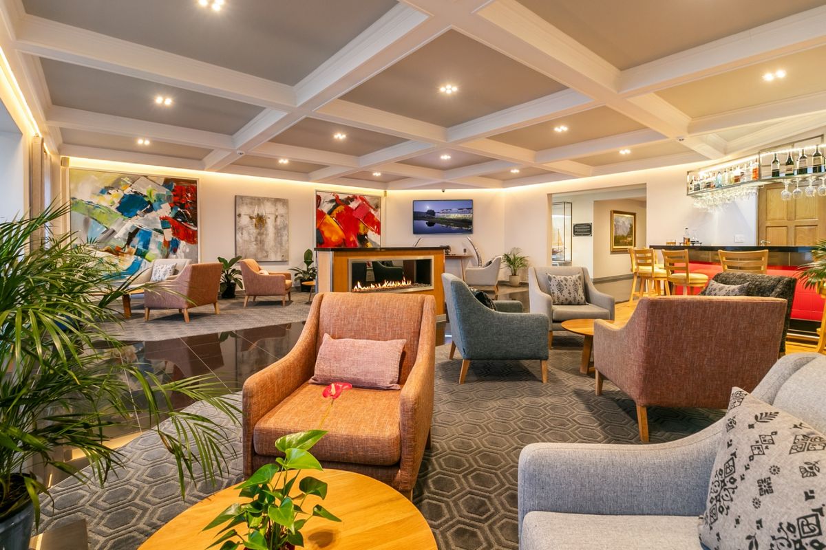 Spacious commercial lounge area featuring a coffered ceiling, recessed lighting, a modern built-in fireplace, and a dedicated bar counter.
