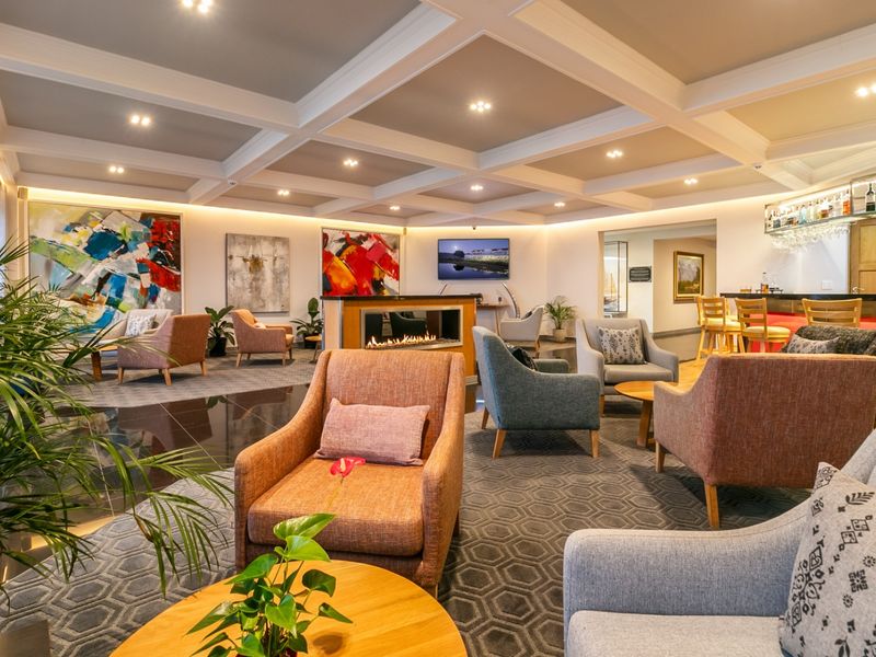 Spacious commercial lounge area featuring a coffered ceiling, recessed lighting, a modern built-in fireplace, and a dedicated bar counter.