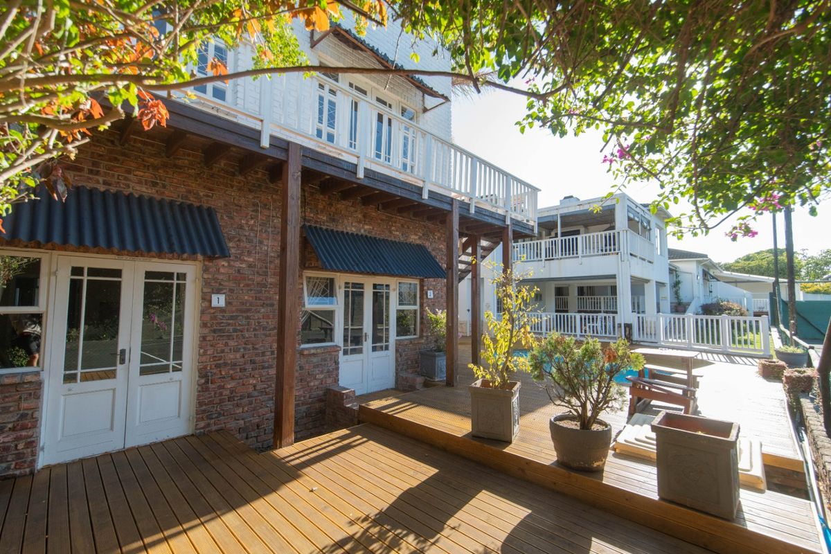 Rear exterior view featuring a multi-level timber deck, exposed brick facade, upper balcony with white railings, and a swimming pool area.